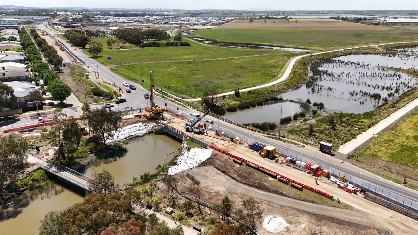 Aerial view of road and bridge works beside wetlands on a growing Victorian corridor