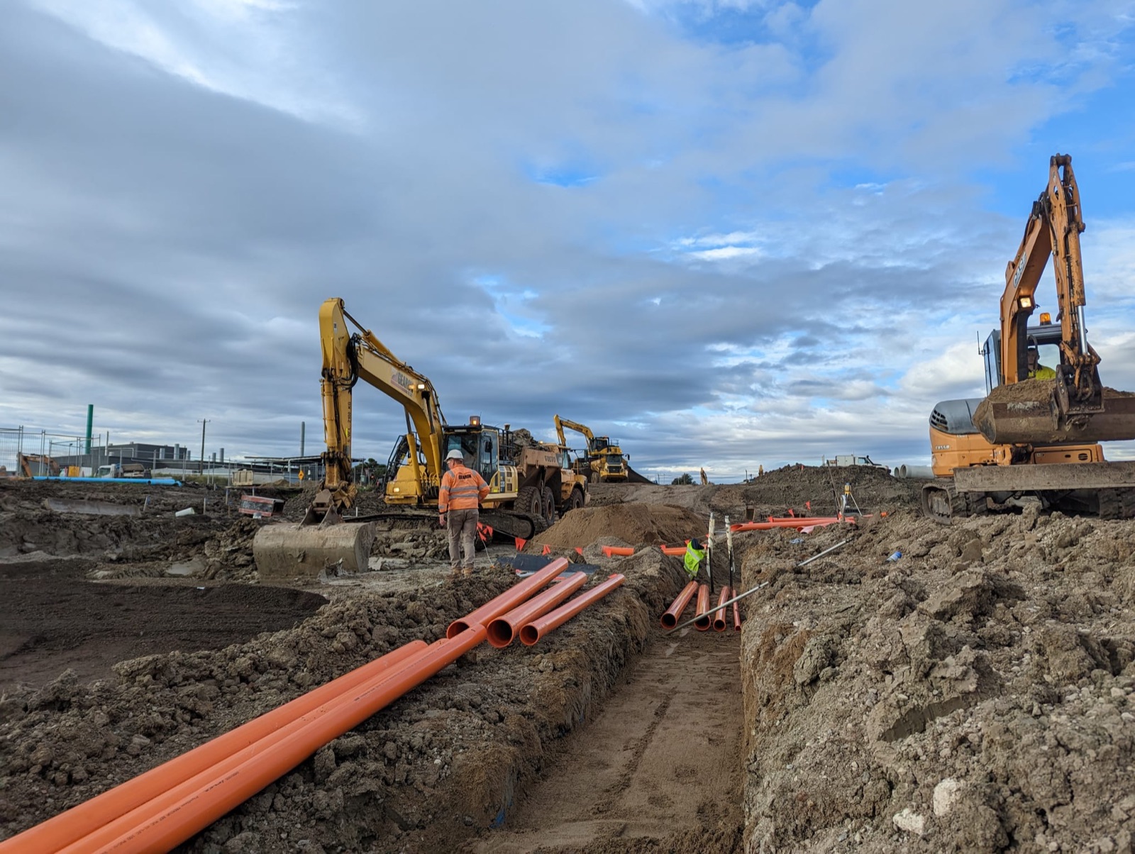 Crew and excavators laying conduit runs on a civil earthworks site