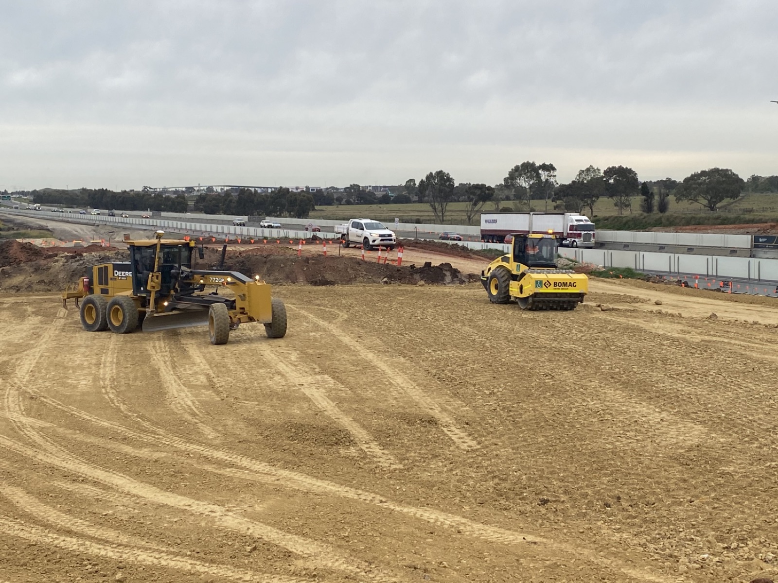 Grader and roller preparing earthworks beside a live Victorian freeway